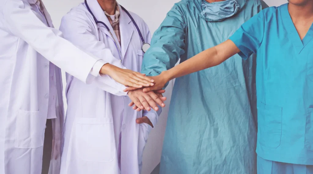 4 oameni îmbrăcați cu uniforme pentru personal medical, ținând mâinile împreunate